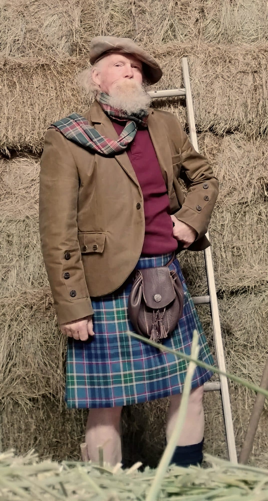 A customer in tweed and kilt beside stacked hay