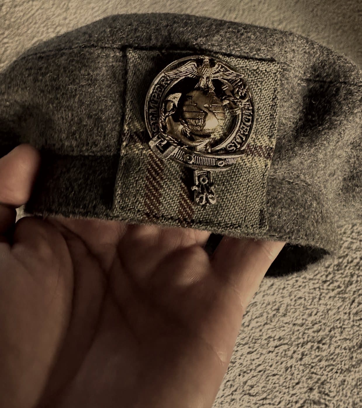 A wool bonnet held in hand, showing the cap badge and the stitched tartan patch